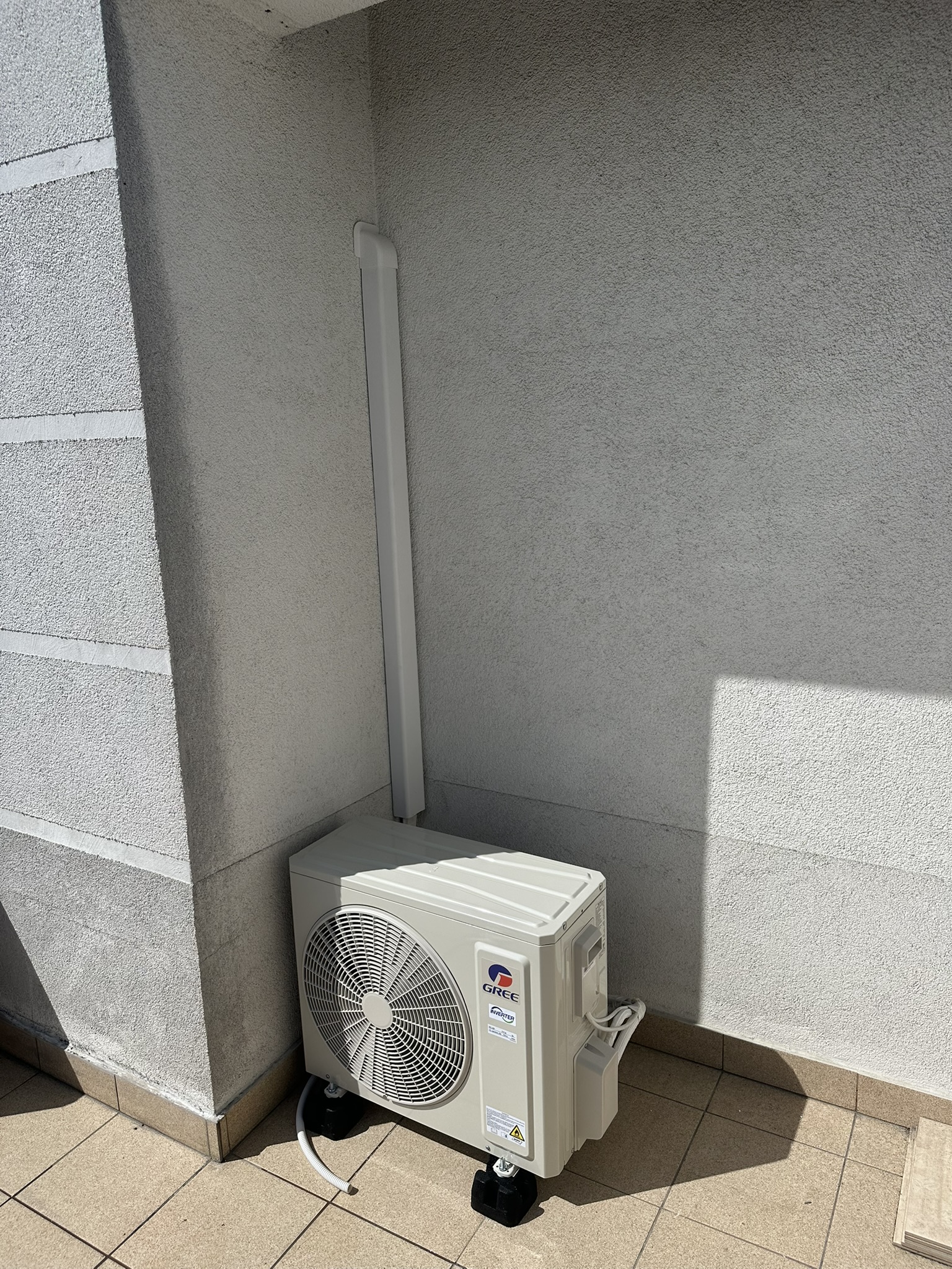 Jednostka zewnętrzna klimatyzatora Gree na podstawach, z instalacją w białym korytku.