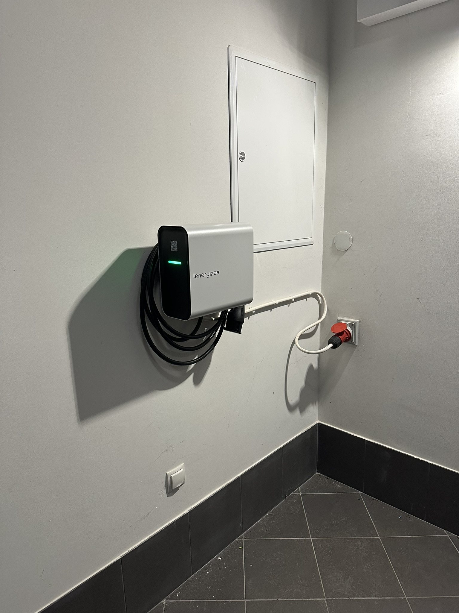 Wallbox na ścianie obok zamkniętej rozdzielnicy i gniazda zasilającego.