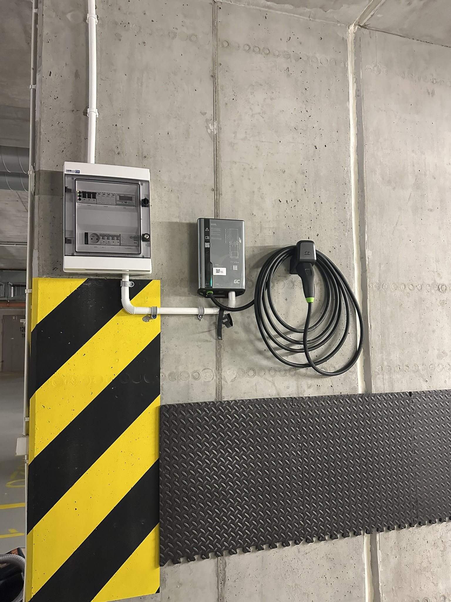 Wallbox i rozdzielnica na betonowej ścianie przy stanowisku w garażu podziemnym.